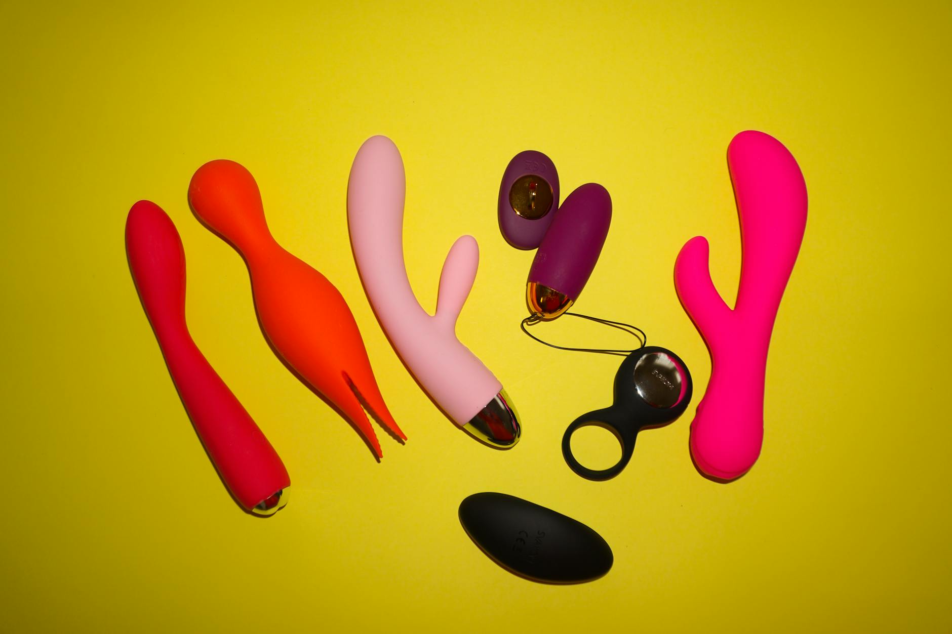 Colorful sex toys arranged on a bright yellow background showcasing intimate wellness design